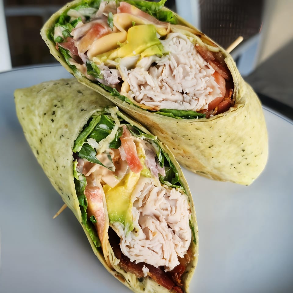 Two halves of a Shorty's American turkey and avocado wrap, filled with lettuce, tomato, and sauce.