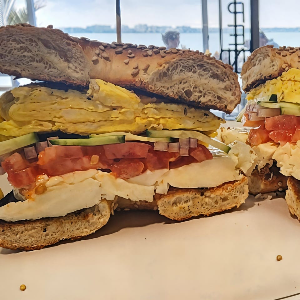 Two Shorty's bagels with egg, cheese, tomato, and cucumber, with a waterfront view.