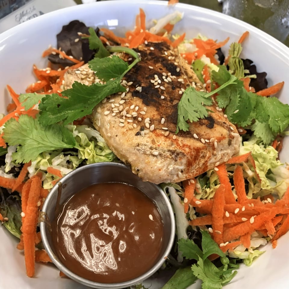 Grilled chicken with sesame seeds, cilantro, shredded carrots, and lettuce, with a side of sauce.