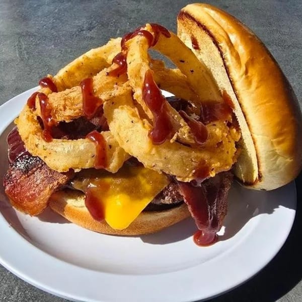 A Shorty's American burger with cheese, bacon, onion rings, and barbecue sauce on a white plate.